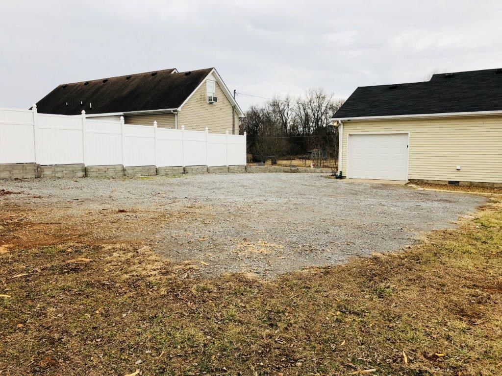 a gravel driveway in front of a house with a white fence