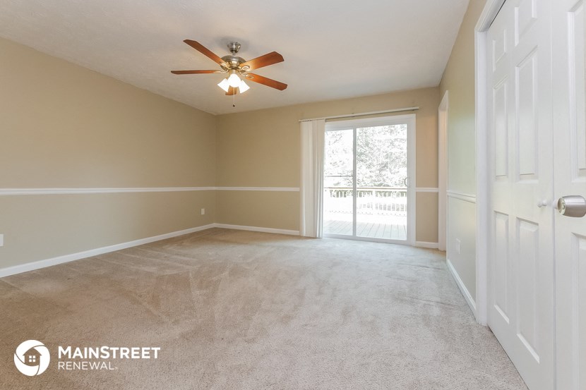 an empty living room with a ceiling fan and a door to a balcony