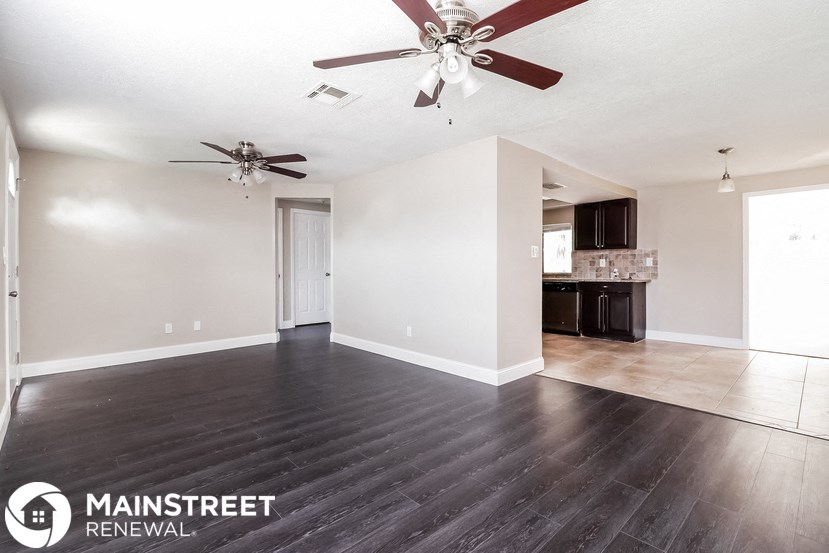 an empty living room with a ceiling fan and a kitchen