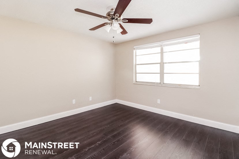the spacious living room with wood flooring and a ceiling fan