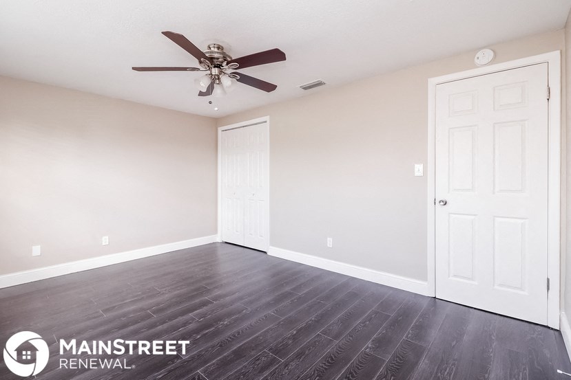 the spacious living room with wood flooring and a ceiling fan