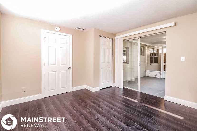 the living room and dining room of an apartment with wood flooring and white doors