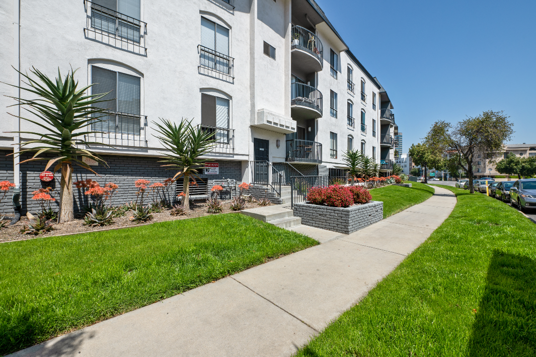 an apartment building with a sidewalk and grass outside of it