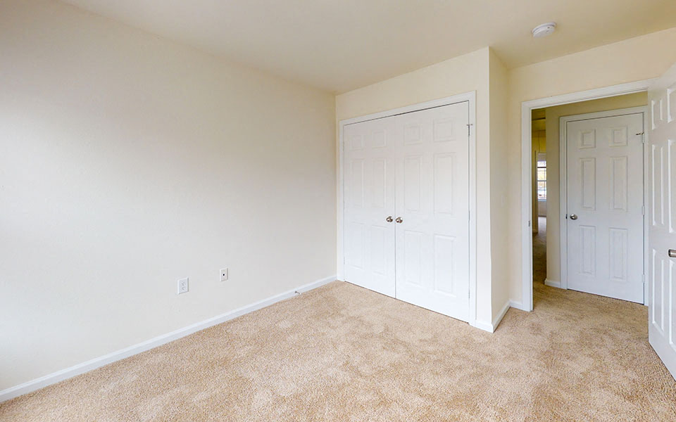 an empty bedroom with a closet and a door to a hallway