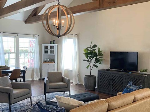 A living room with a brown leather couch, a wooden chandelier, and a television on a cabinet.