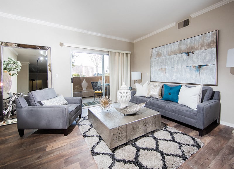 A living room with a grey couch, a grey armchair, a coffee table, and a large abstract painting on the wall.