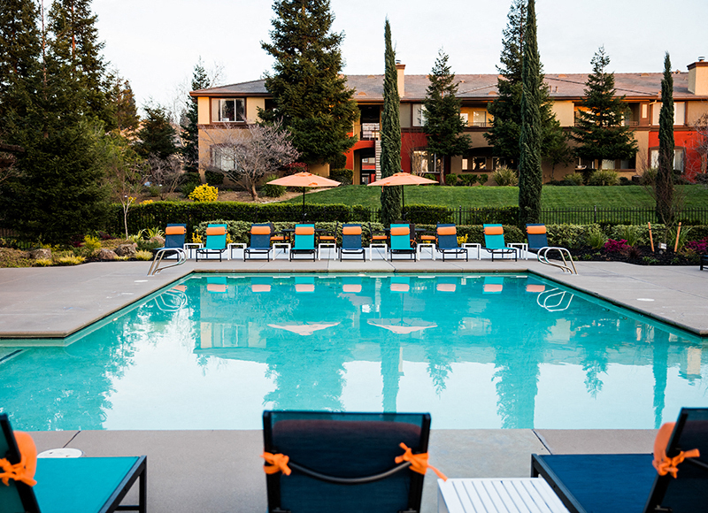 A pool with chairs around it and a building in the background.