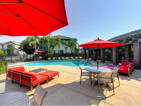 Apartments For Rent In Rocklin - Gated Pool With Shaded Lounge, Chairs, Tables With Umbrellas, And Palm Trees.
