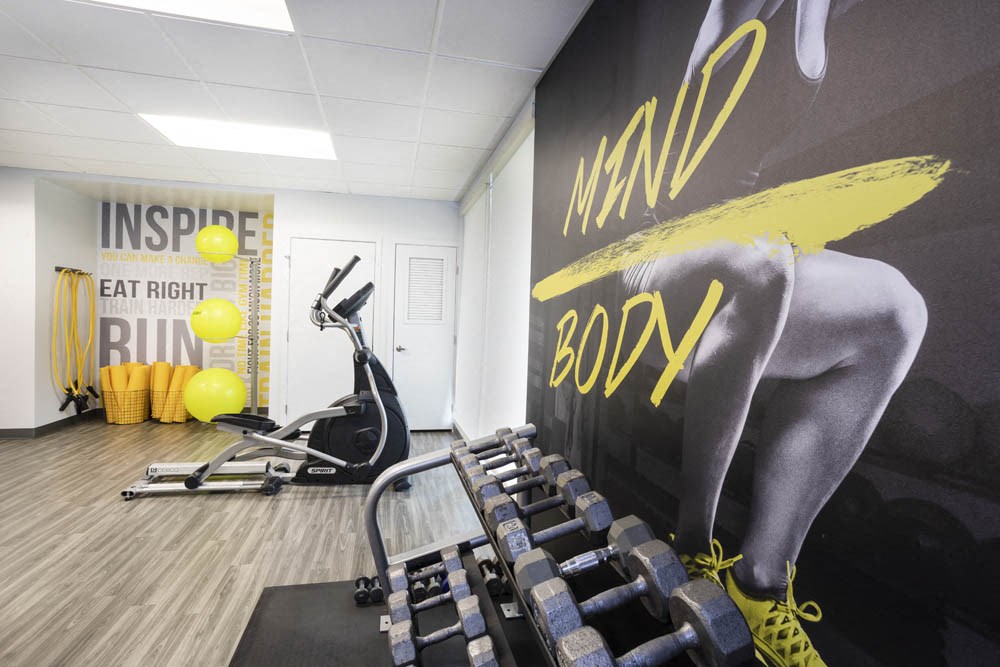 a gym with cardio equipment and a wall mural of a woman in a workout room