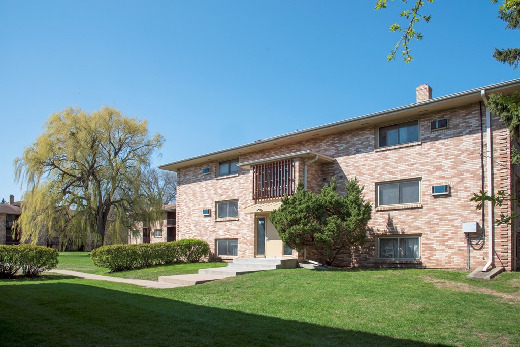 a brick apartment building with a green lawn and a blue sky