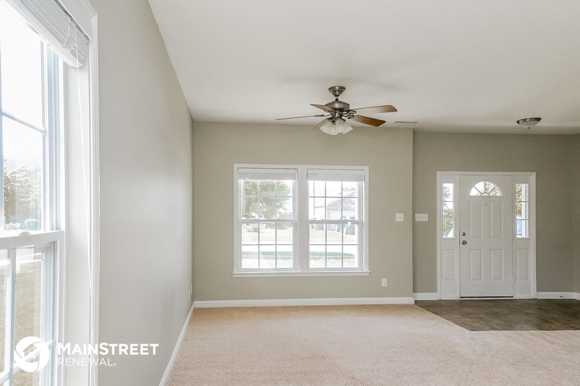 an empty living room with a ceiling fan and two windows