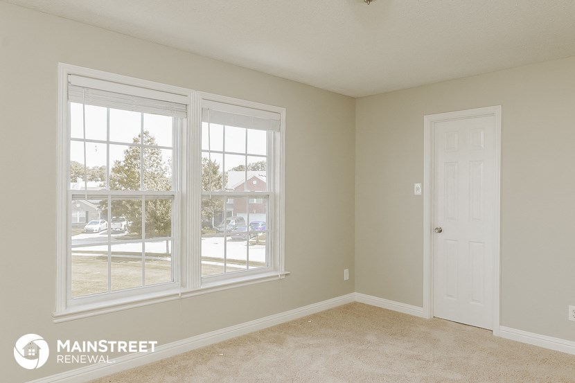 a bedroom with three large windows and a white door