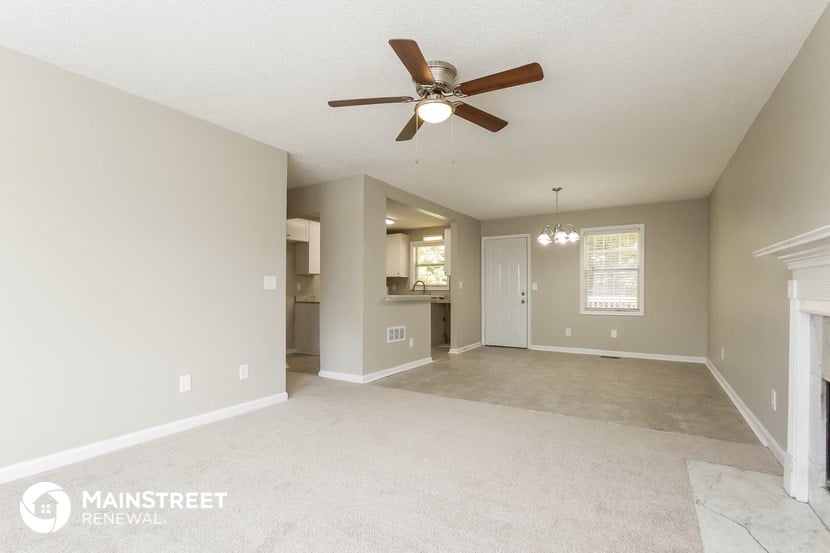 an empty living room with a ceiling fan and a kitchen