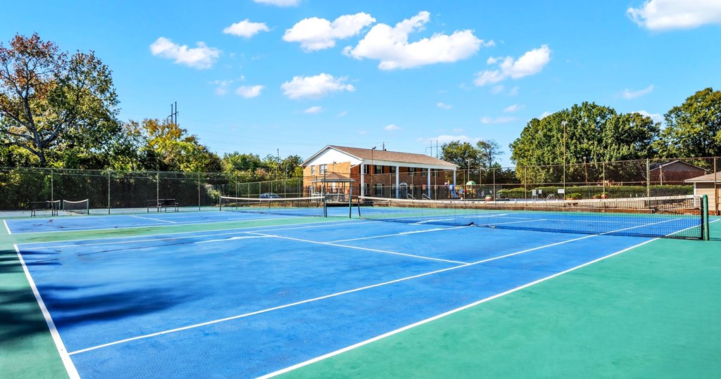 A tennis court with a blue surface and white lines, surrounded by a fence and trees.