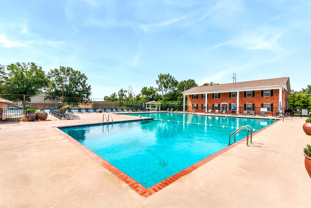 A large outdoor swimming pool with a red border and a building in the background.