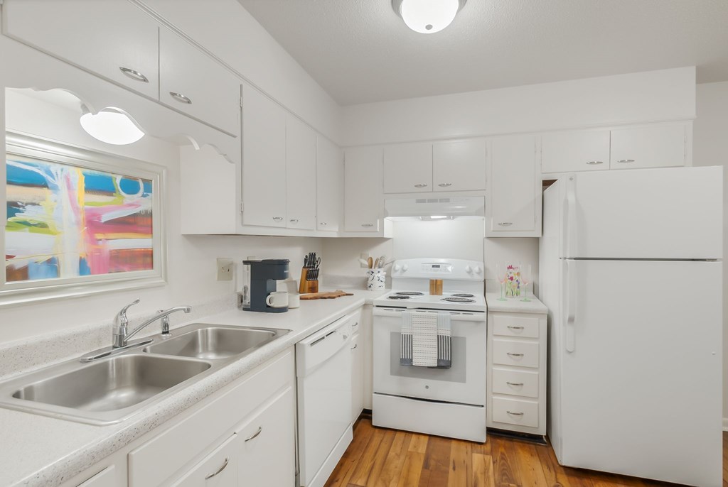 A white kitchen with a stove, sink, and refrigerator.
