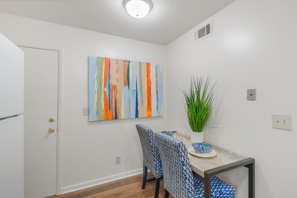 A dining room with a table set for two and a painting on the wall.