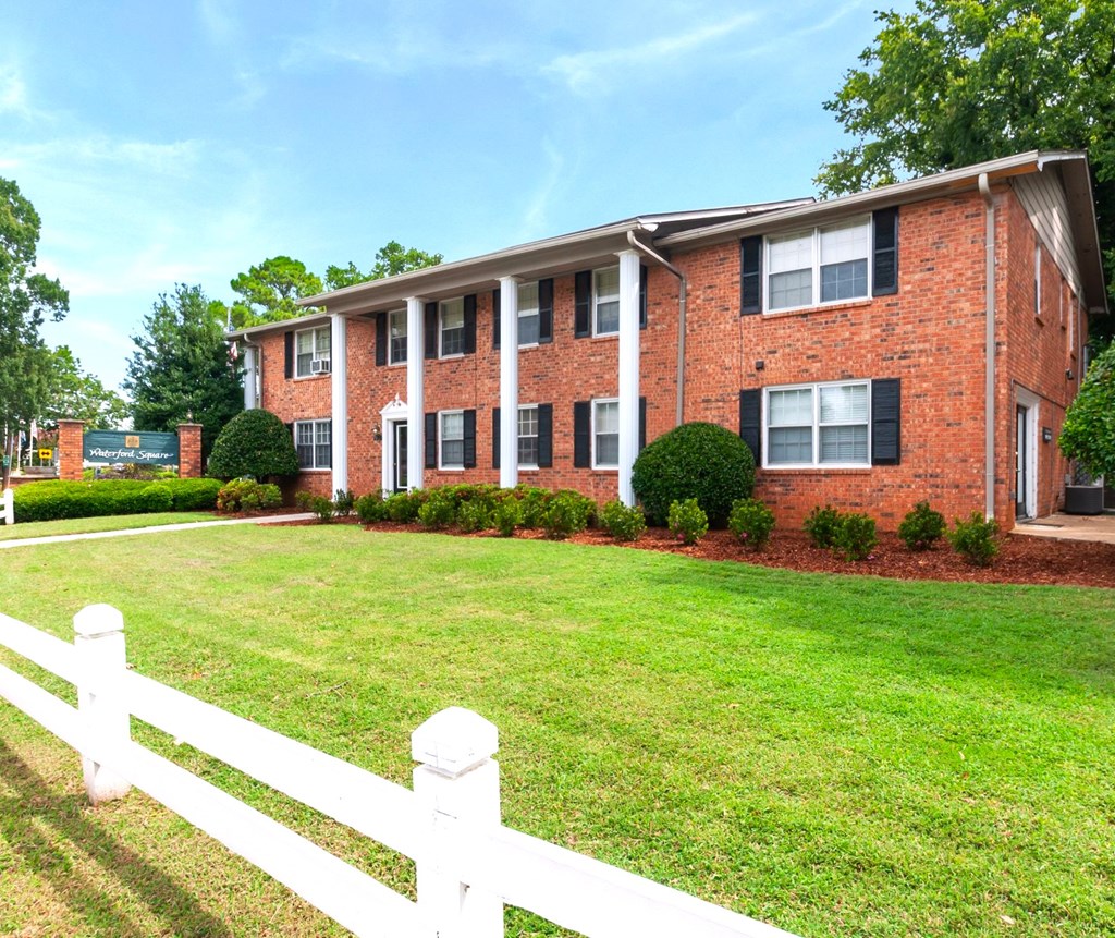 A red brick apartment building with a white picket fence in front.