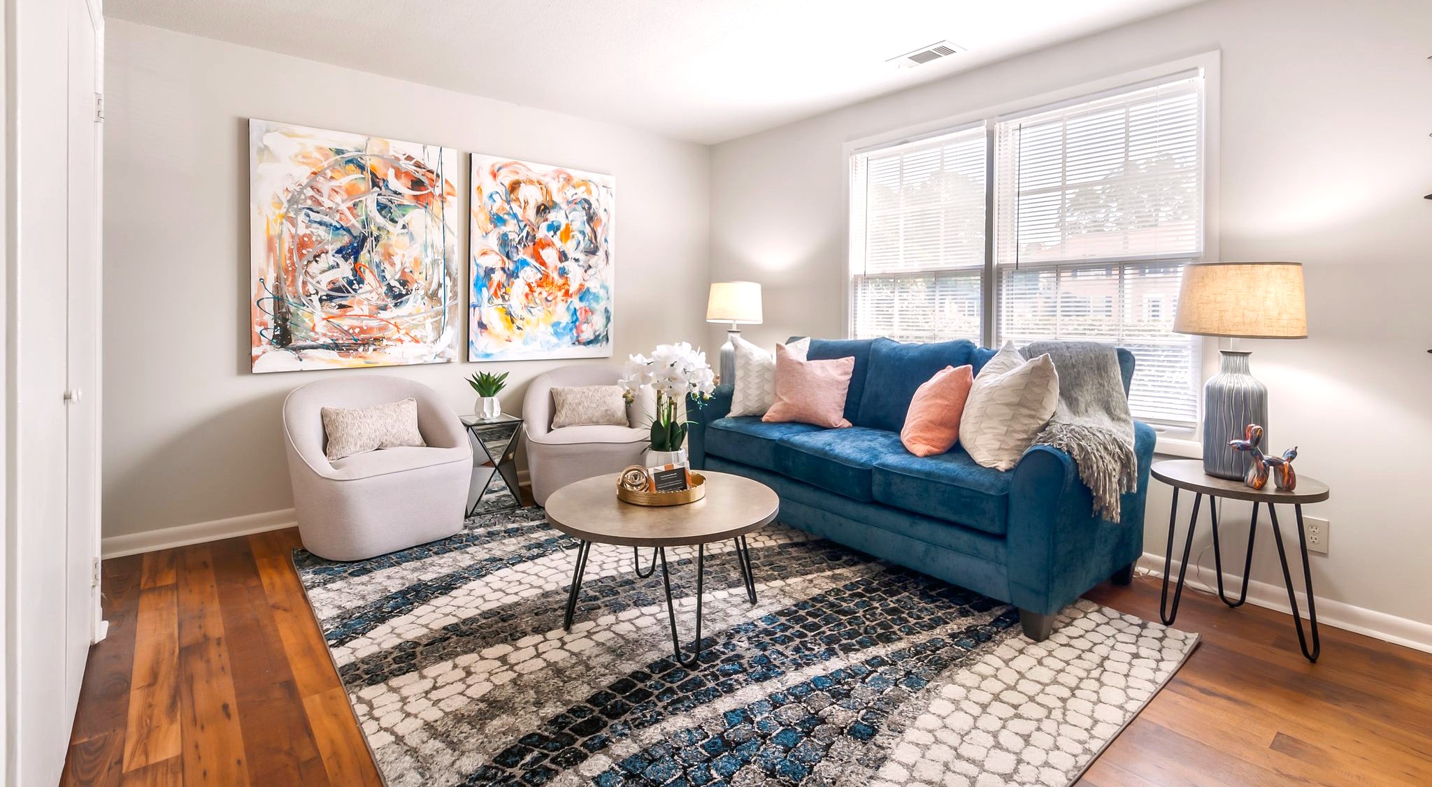 A living room with a blue couch, a white chair, and a coffee table with a vase of flowers on it.