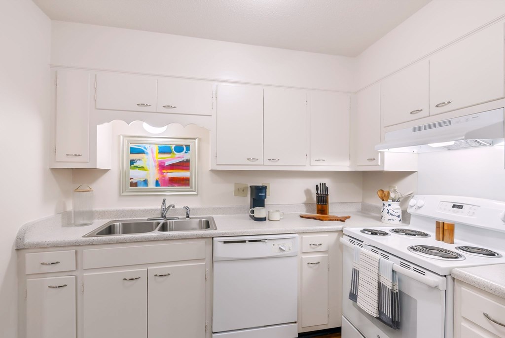 A white kitchen with a stove, sink, and cabinets.