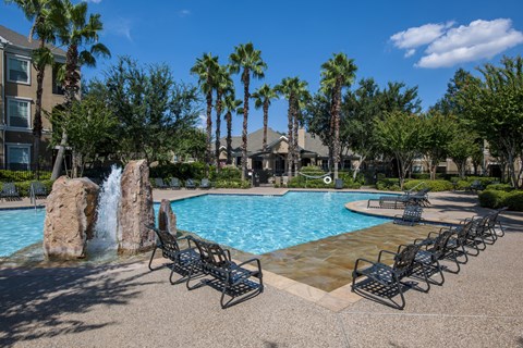 A pool with a waterfall and lounge chairs.