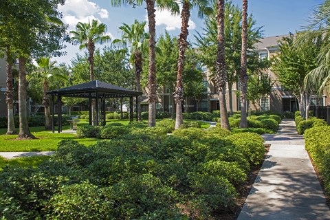 A gazebo is surrounded by green bushes and trees.