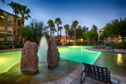 A pool with a waterfall and a bench.