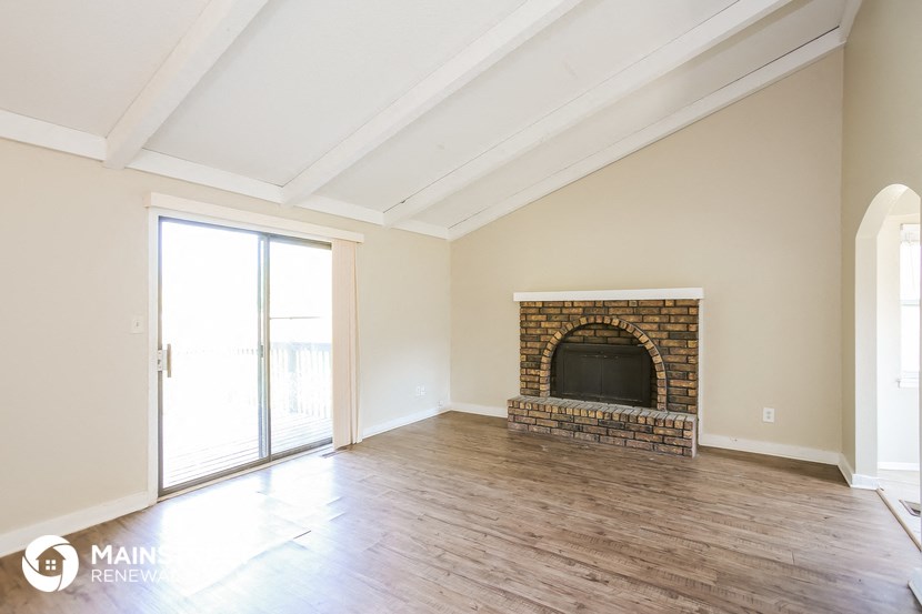 an empty living room with a brick fireplace and wooden floors