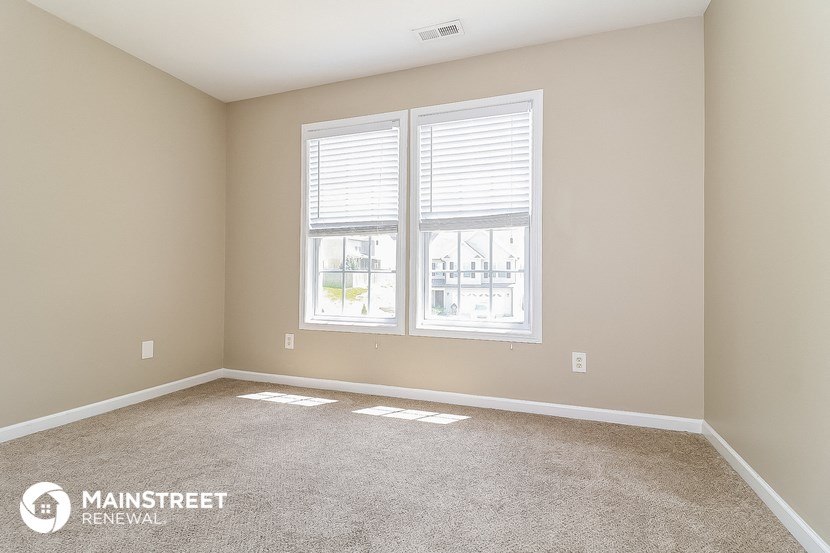 the spacious living room with two windows and carpeting