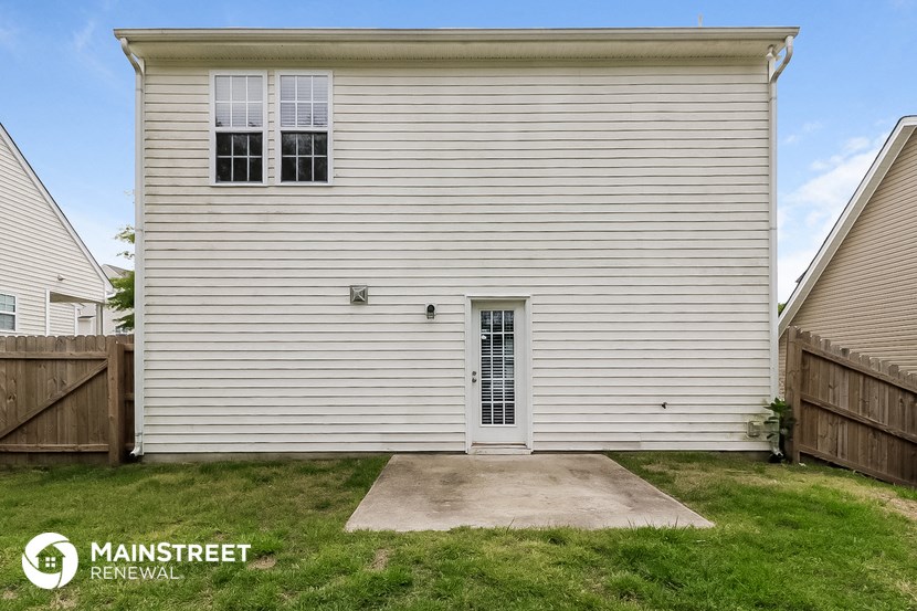 the side of a white house with a driveway and grass