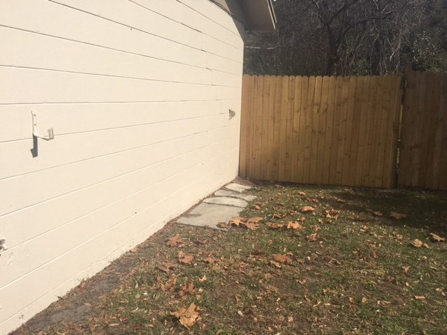 the side of a house with a sidewalk next to a fence