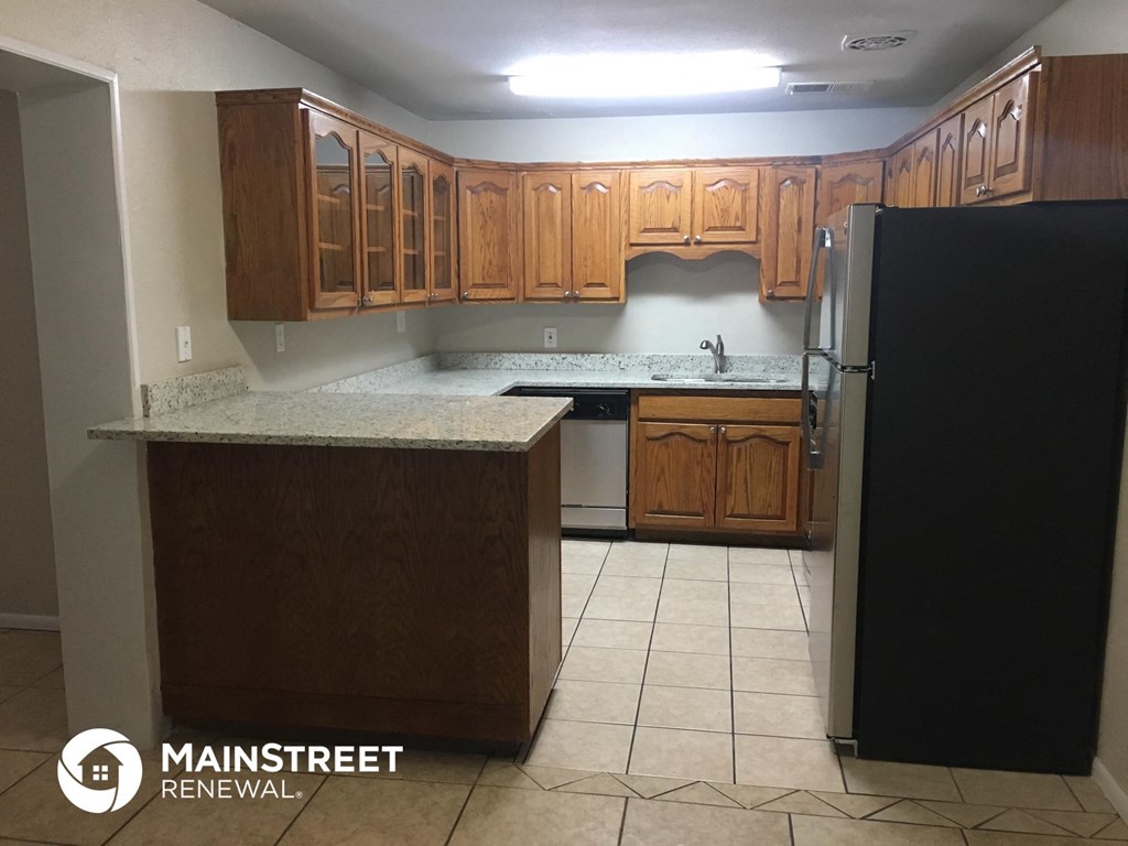 an empty kitchen with wooden cabinets and a black refrigerator