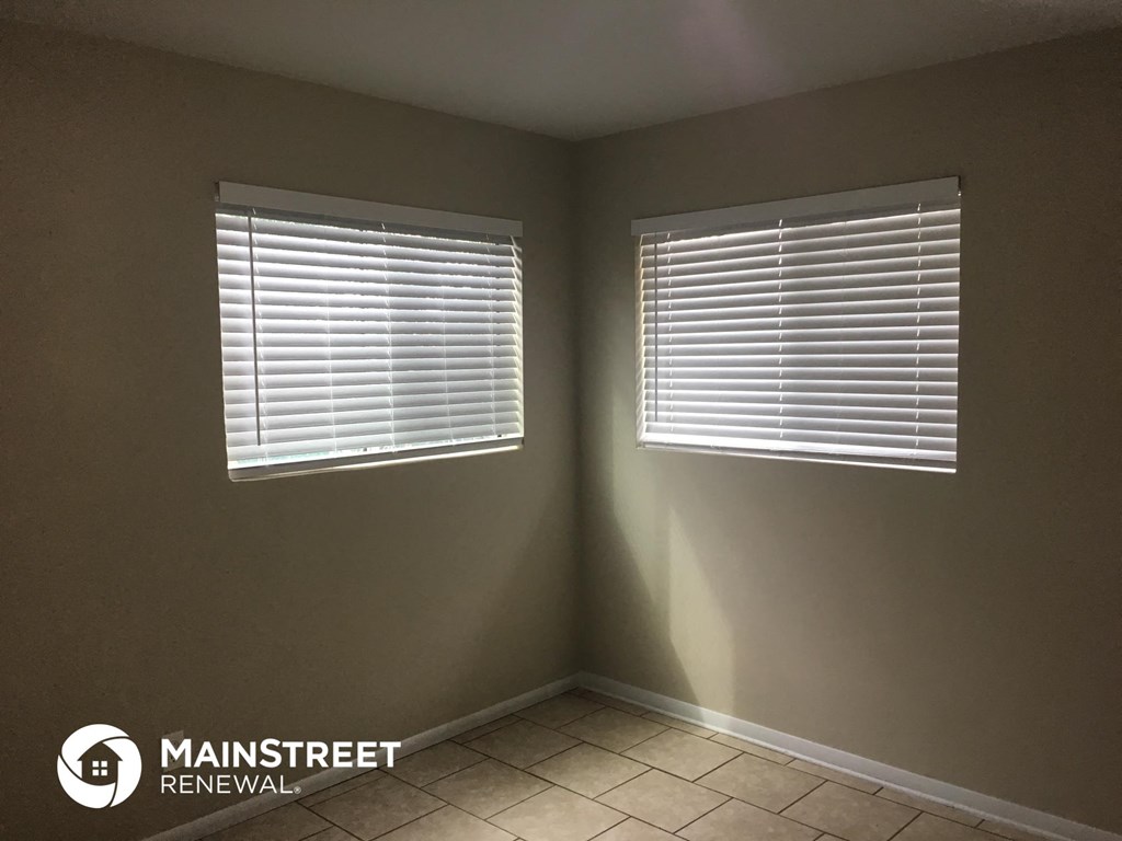two windows with blinds in a room with a tiled floor
