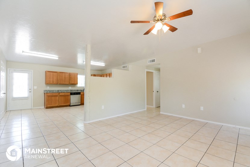 an empty living room with a ceiling fan and a kitchen