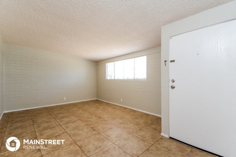 the spacious living room of a home with tile flooring and a window