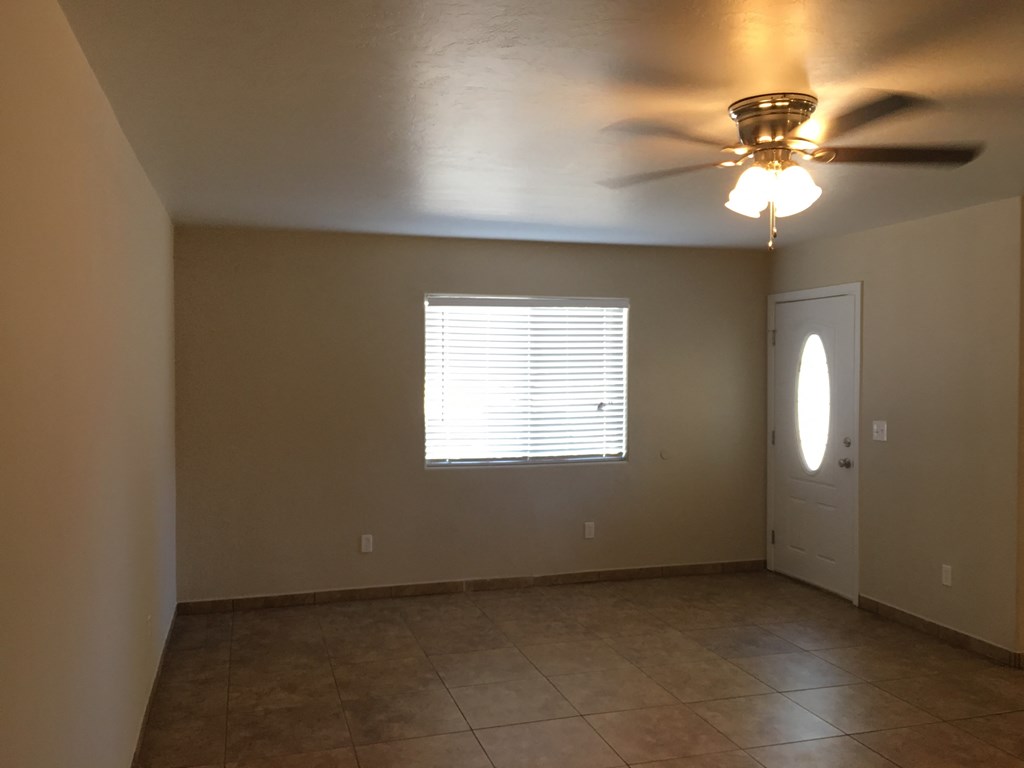 an empty living room with a ceiling fan and a door
