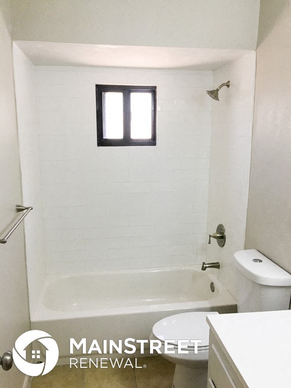 a white bathroom with a tub and a toilet and a window