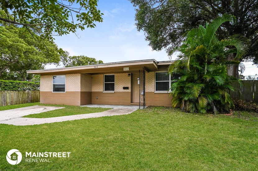 a small tan house with a yard and palm tree