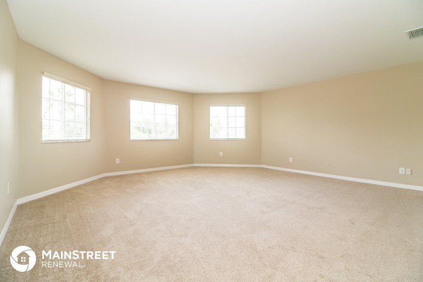 the spacious living room with carpeting and three windows