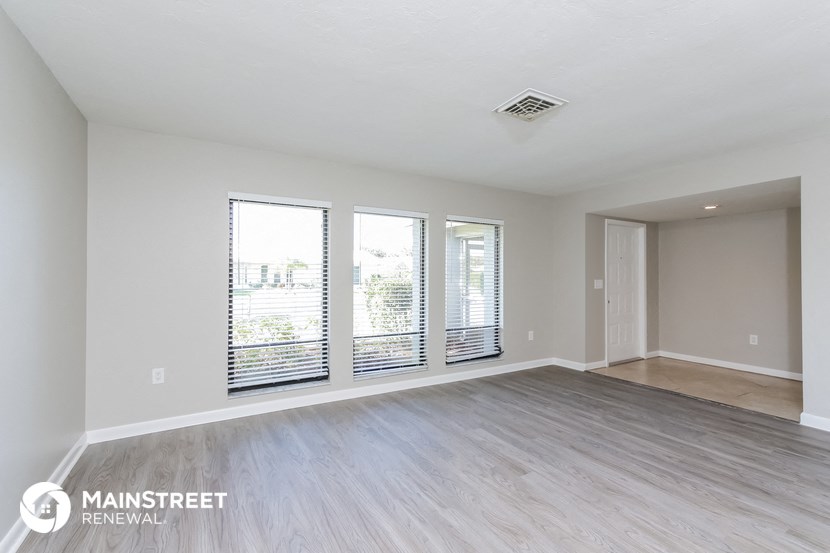 an empty living room with wood flooring and large windows
