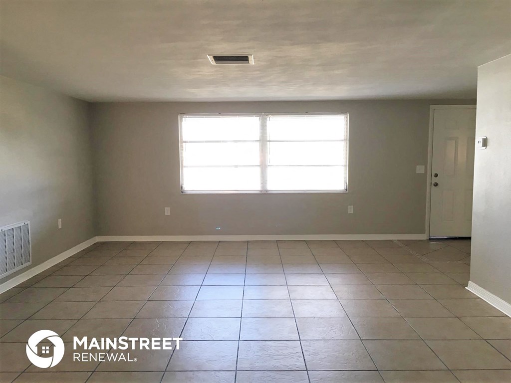 an empty living room with a window and a tiled floor