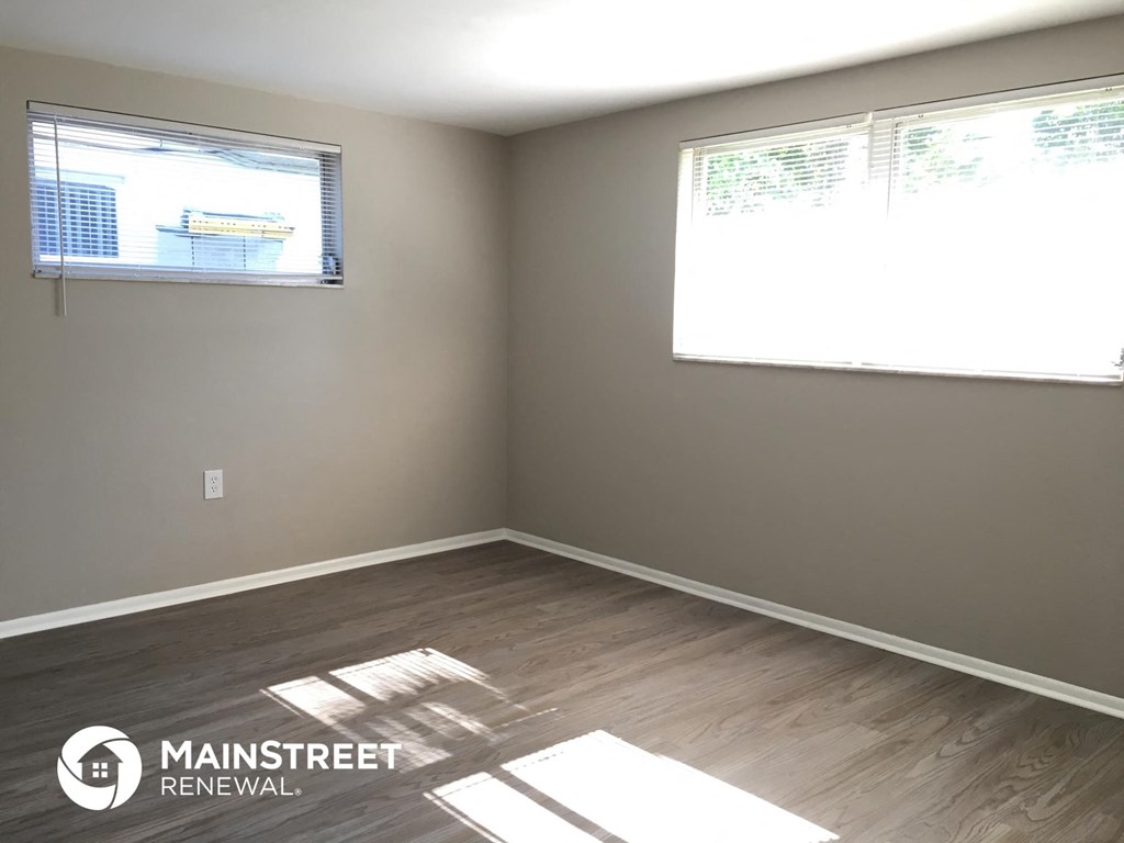 an empty room with wood floors and two windows