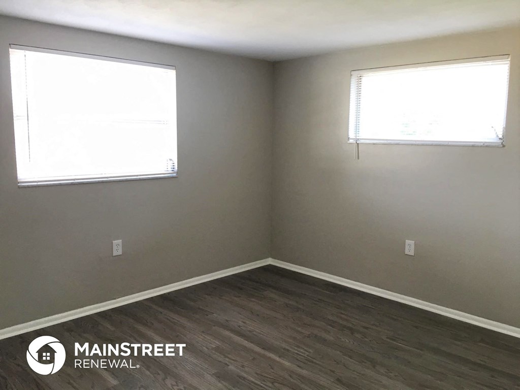 an empty room with two windows and a wooden floor