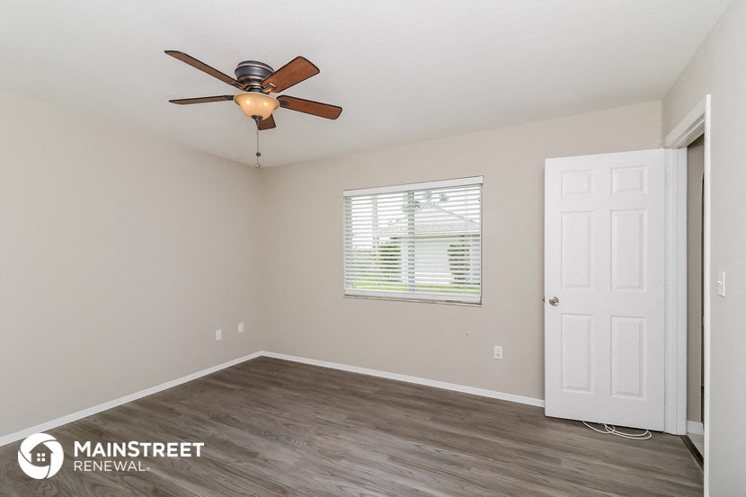the spacious living room with a ceiling fan and a white door