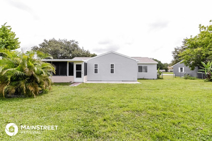 a small gray house with a yard and a palm tree