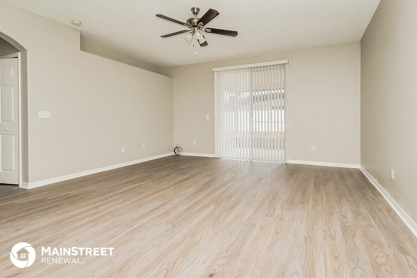 the spacious living room with wood flooring and a ceiling fan