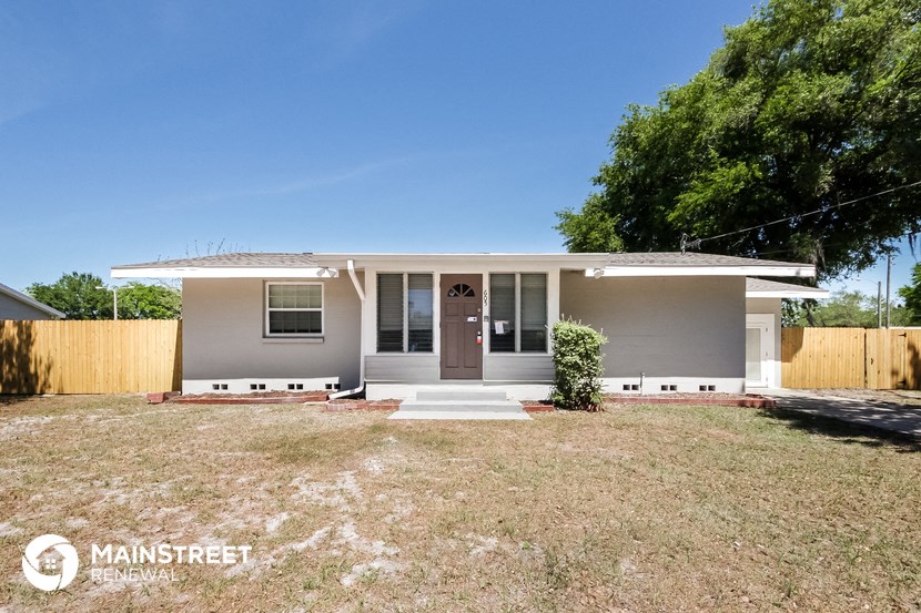 a small gray house with a yard and a wooden fence