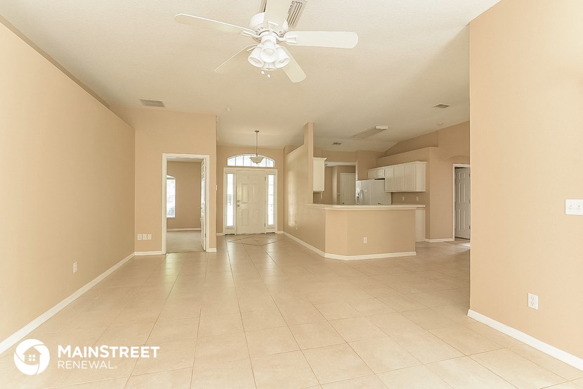 an empty living room with a ceiling fan and a kitchen