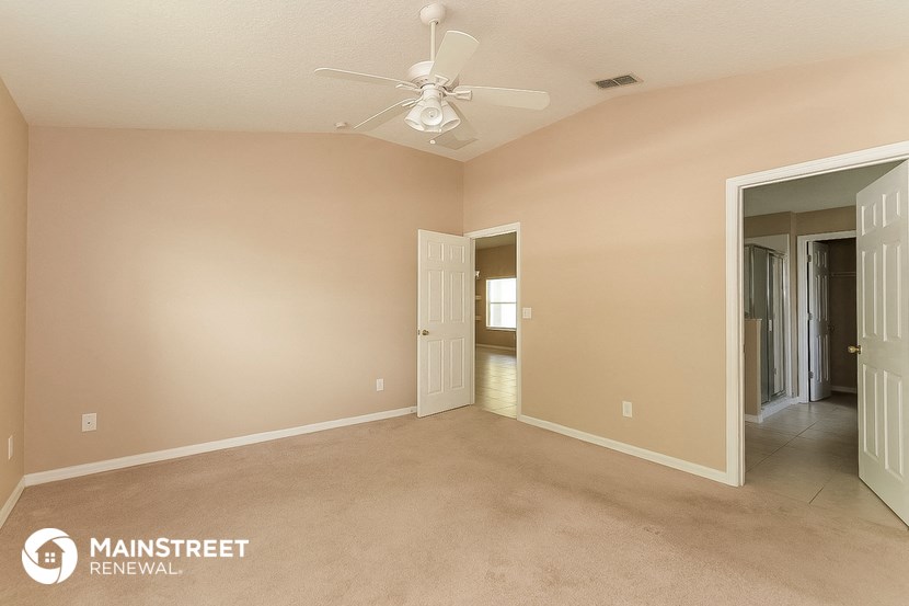 a empty living room with a ceiling fan and a door to a hallway