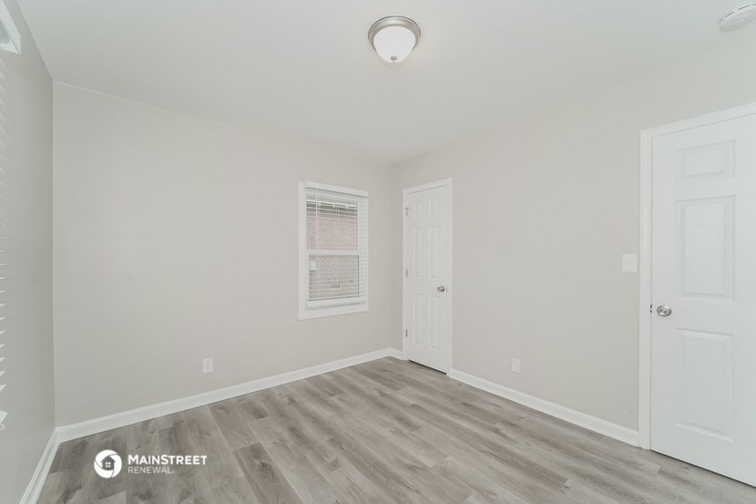 a bedroom with white walls and wood flooring and a white door